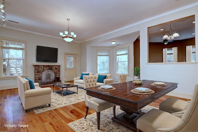 dining area with ornamental molding, a chandelier, light hardwood / wood-style flooring, and a stone fireplace