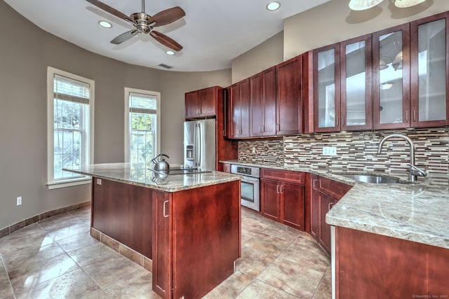 kitchen with sink, light stone countertops, appliances with stainless steel finishes, and a center island