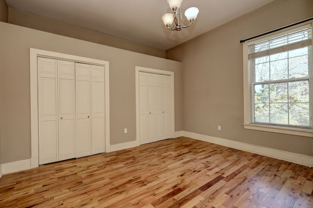 unfurnished bedroom featuring multiple closets, a chandelier, and light wood-type flooring