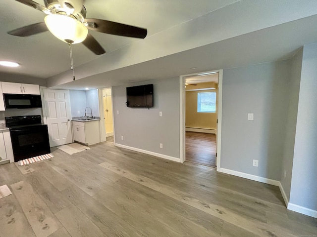 unfurnished living room featuring ceiling fan, light wood-type flooring, sink, and a baseboard heating unit