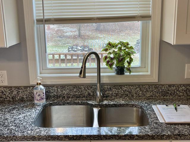 interior details featuring dark stone countertops, white cabinetry, and sink