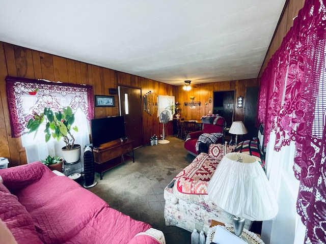 living room with wooden walls, ceiling fan, and dark colored carpet