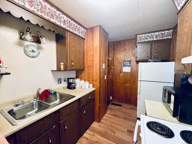 kitchen with white appliances, sink, wooden walls, light hardwood / wood-style floors, and dark brown cabinetry