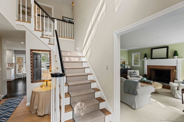 staircase with wood-type flooring, ornamental molding, and a brick fireplace