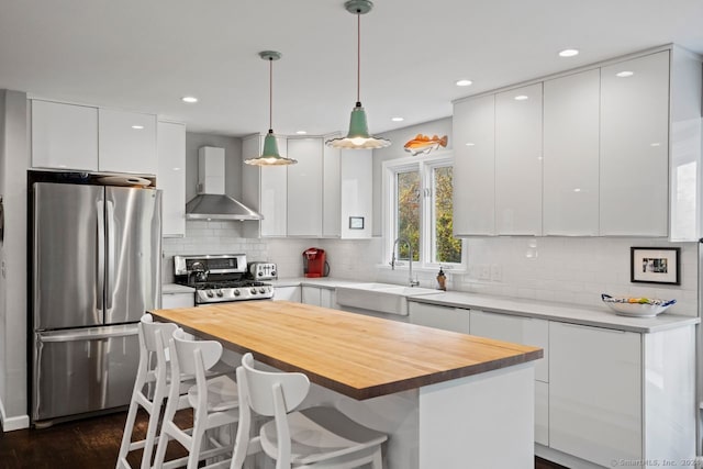 kitchen featuring sink, wall chimney exhaust hood, hanging light fixtures, stainless steel appliances, and white cabinets