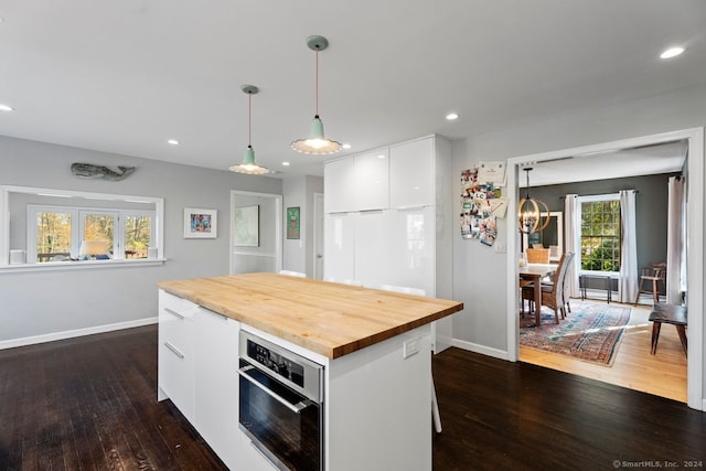 kitchen featuring pendant lighting, a center island, oven, dark hardwood / wood-style flooring, and white cabinetry