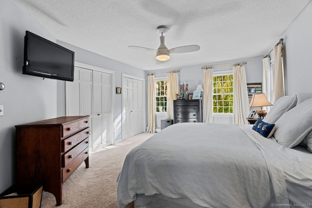 carpeted bedroom with a textured ceiling, two closets, and ceiling fan