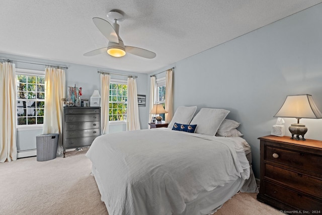 carpeted bedroom with a textured ceiling, multiple windows, a baseboard heating unit, and ceiling fan