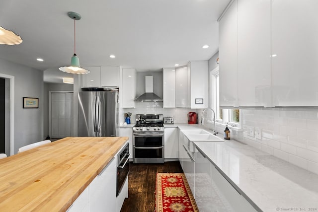 kitchen with wall chimney exhaust hood, dark wood-type flooring, stainless steel appliances, decorative light fixtures, and white cabinets