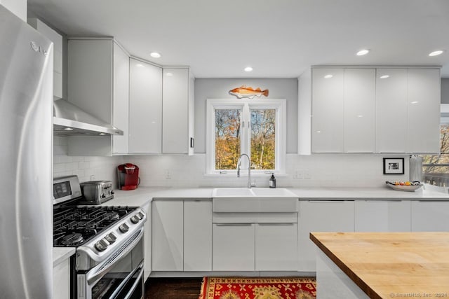 kitchen with backsplash, wall chimney exhaust hood, stainless steel appliances, sink, and white cabinetry