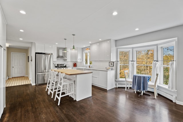 kitchen featuring white cabinetry, wall chimney range hood, hanging light fixtures, and appliances with stainless steel finishes