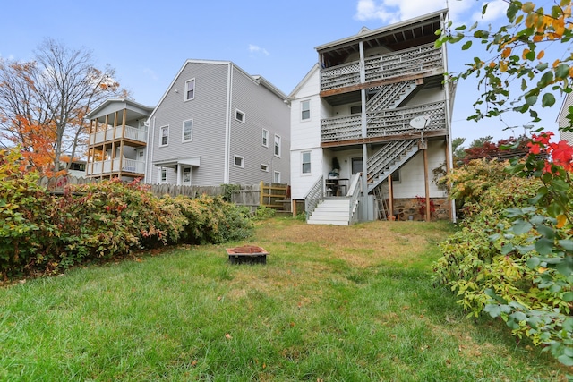 back of house featuring a balcony, an outdoor fire pit, and a lawn