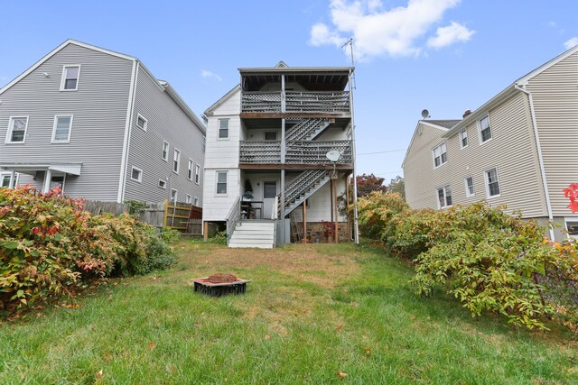 rear view of property with a balcony, a yard, and an outdoor fire pit