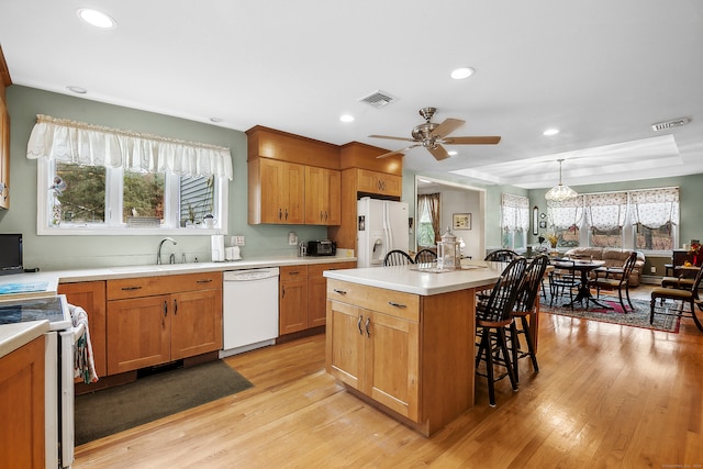 kitchen with a healthy amount of sunlight, a kitchen island, light hardwood / wood-style floors, and white appliances