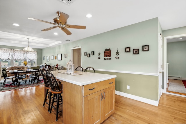 kitchen featuring a kitchen island, a breakfast bar area, pendant lighting, a baseboard radiator, and light hardwood / wood-style floors