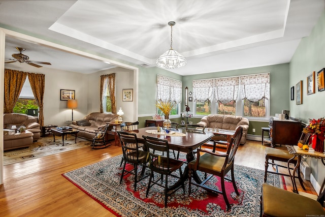 dining room featuring baseboard heating, hardwood / wood-style flooring, a raised ceiling, and ceiling fan with notable chandelier