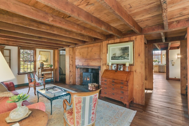 living room featuring beam ceiling, a wood stove, dark wood-type flooring, and a healthy amount of sunlight