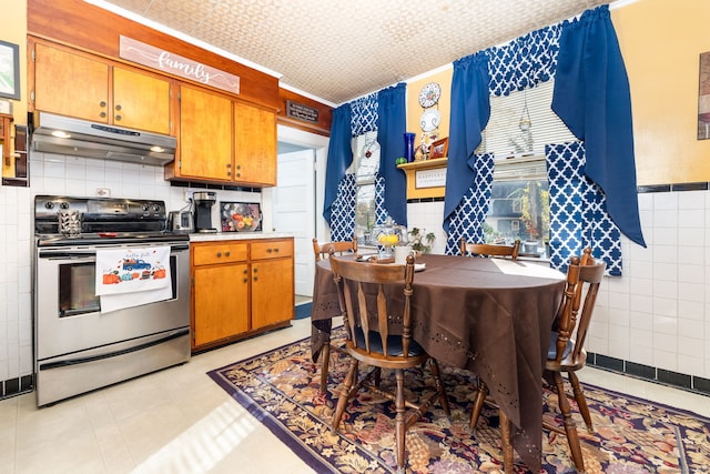 kitchen with under cabinet range hood, stainless steel electric range, brown cabinetry, tile walls, and light countertops