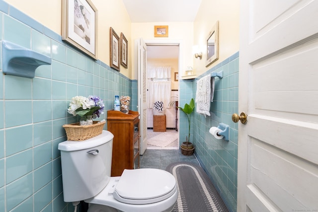 bathroom featuring tile walls, tile patterned floors, toilet, and wainscoting