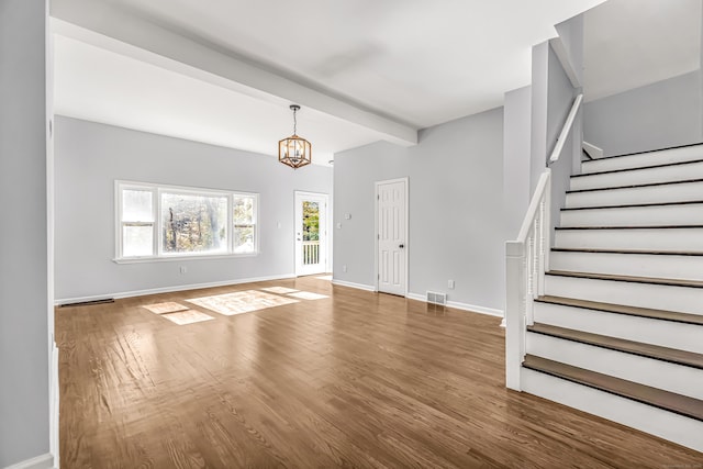 unfurnished living room featuring beam ceiling, hardwood / wood-style floors, and a chandelier