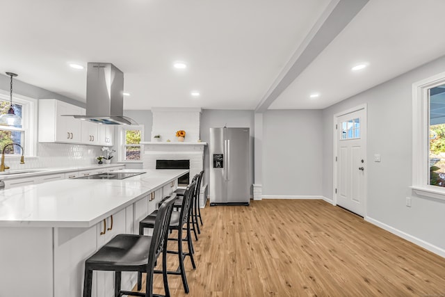 kitchen with island range hood, stainless steel fridge, sink, white cabinetry, and light hardwood / wood-style floors