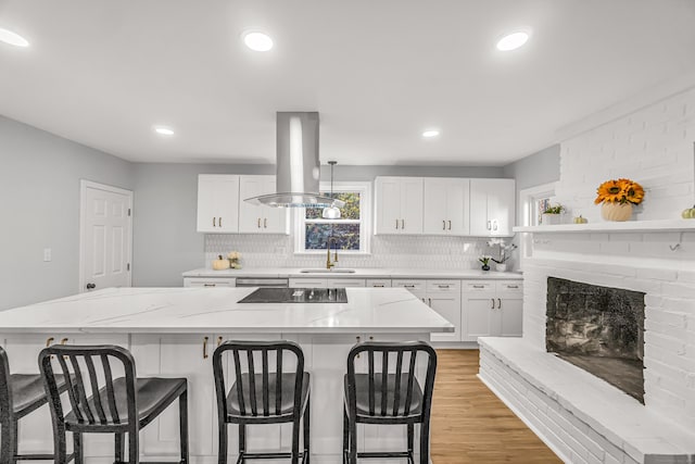 kitchen featuring island range hood, a center island, white cabinetry, light hardwood / wood-style floors, and light stone counters