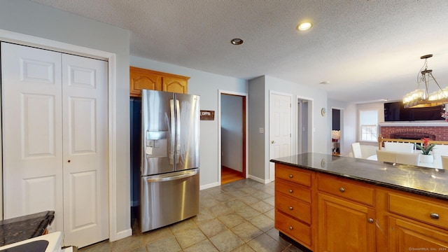 kitchen with a fireplace, stainless steel refrigerator with ice dispenser, a textured ceiling, and hanging light fixtures