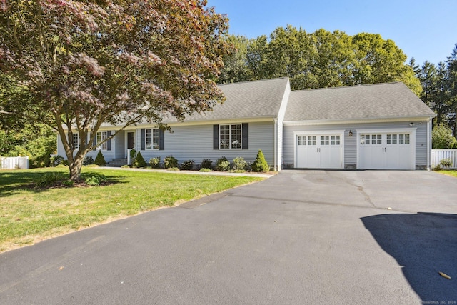 view of front facade with a front lawn, aphalt driveway, fence, an attached garage, and a shingled roof