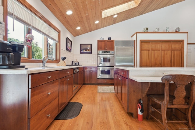 kitchen featuring wood ceiling, light countertops, light wood-style flooring, vaulted ceiling with skylight, and appliances with stainless steel finishes