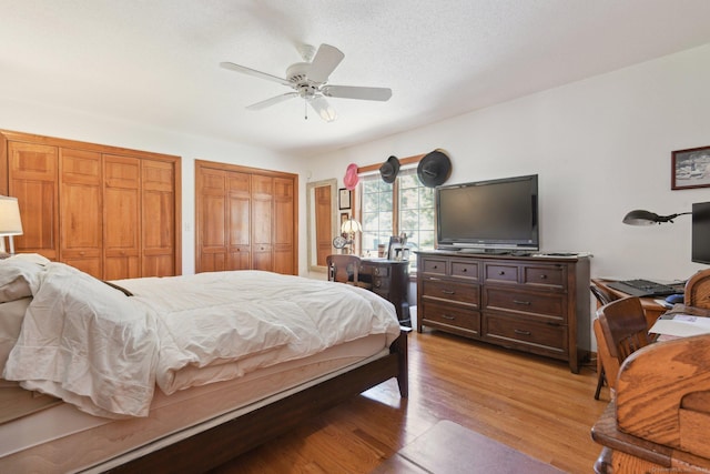 bedroom with light wood-type flooring, two closets, a ceiling fan, and a textured ceiling