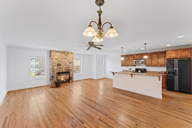 kitchen with a stone fireplace, black appliances, a breakfast bar, light stone countertops, and light hardwood / wood-style flooring