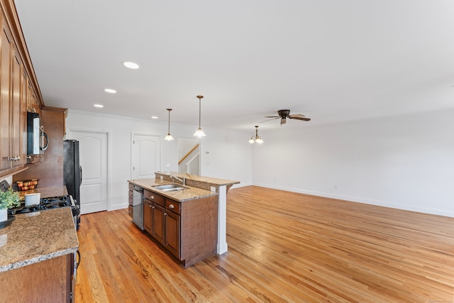 kitchen with stainless steel appliances, sink, an island with sink, pendant lighting, and light wood-type flooring