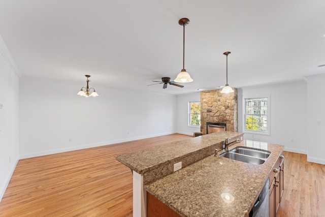 kitchen with a stone fireplace, a center island with sink, sink, light hardwood / wood-style flooring, and decorative light fixtures