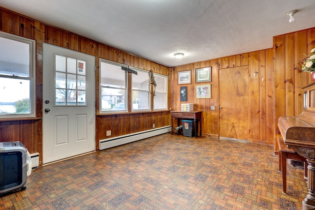 interior space with a textured ceiling, wood walls, and baseboard heating