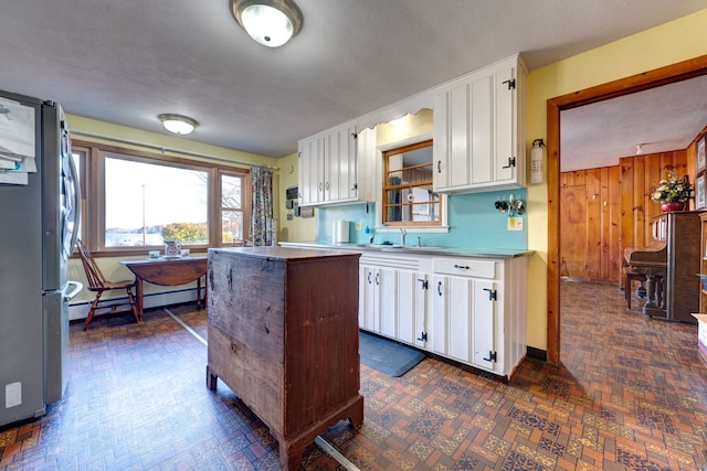 kitchen with a baseboard heating unit, wooden walls, sink, white cabinetry, and stainless steel refrigerator