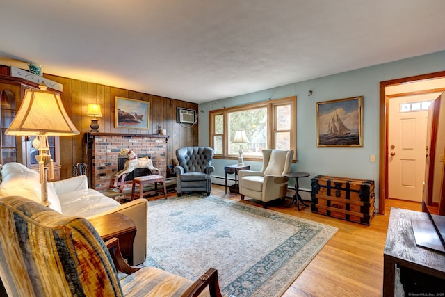 living room featuring light wood-type flooring, wooden walls, a brick fireplace, and a baseboard heating unit