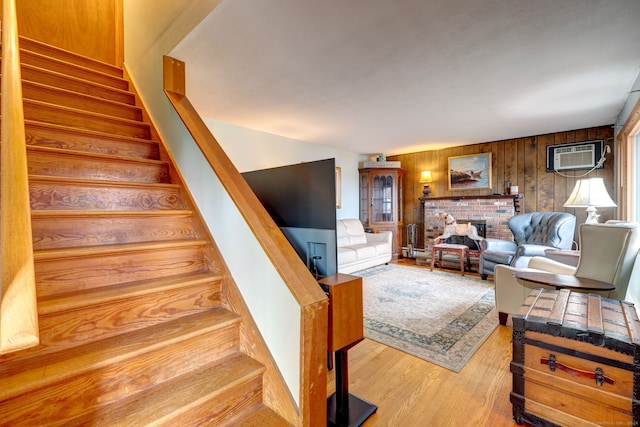 living room featuring a fireplace, light hardwood / wood-style floors, a wall mounted AC, and wooden walls