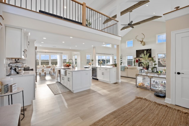 kitchen with a towering ceiling, ceiling fan, sink, a center island with sink, and white cabinetry