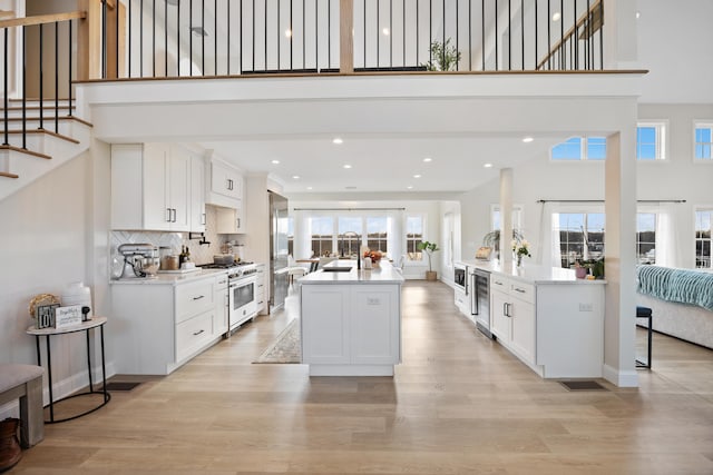 kitchen with high end stove, white cabinetry, a center island with sink, and light wood-type flooring