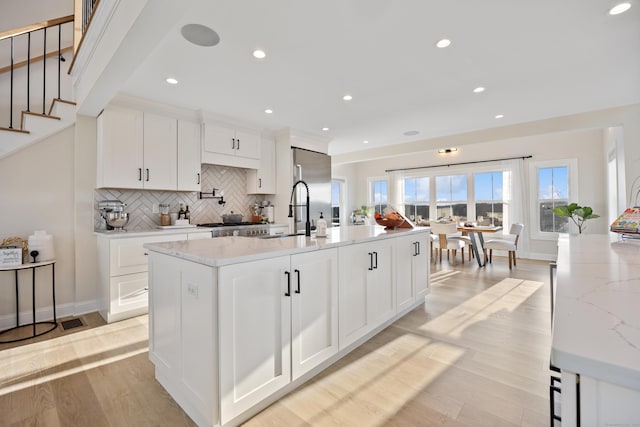 kitchen featuring white cabinetry, sink, light stone counters, an island with sink, and light wood-type flooring