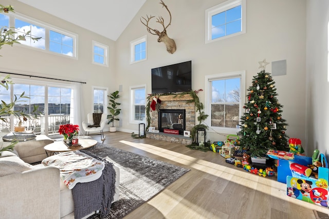 living room with a stone fireplace, wood-type flooring, and a towering ceiling