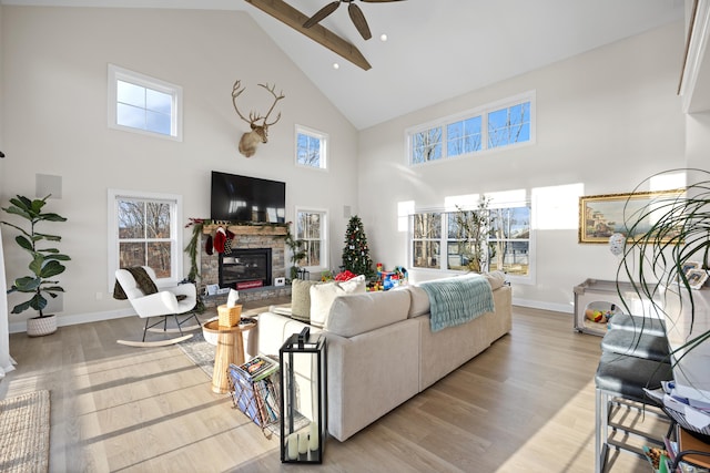 living room with ceiling fan, a fireplace, light hardwood / wood-style floors, and a high ceiling