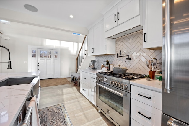 kitchen with sink, stainless steel appliances, tasteful backsplash, light stone counters, and white cabinets