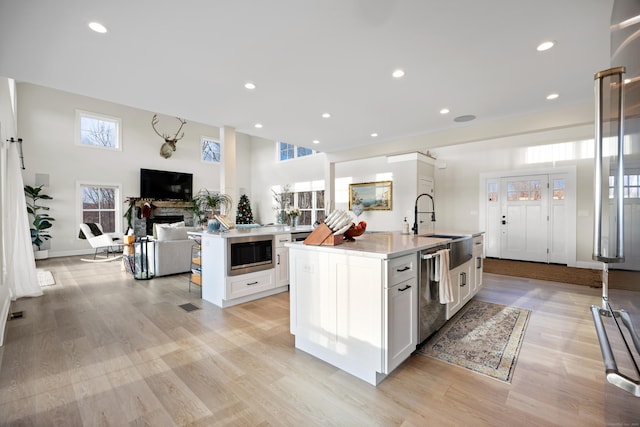 kitchen featuring built in microwave, white cabinetry, dishwasher, a center island with sink, and light wood-type flooring