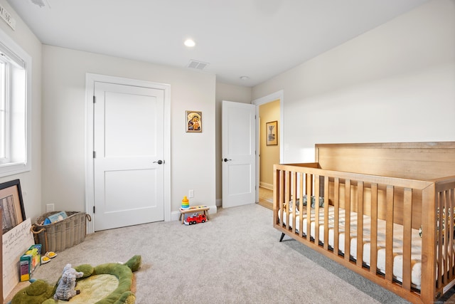 bedroom with multiple windows, light colored carpet, and a crib