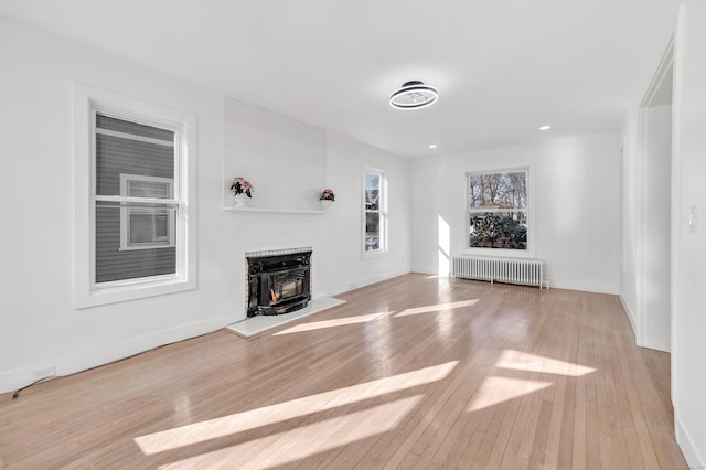 unfurnished living room featuring light wood-type flooring, a wood stove, and radiator