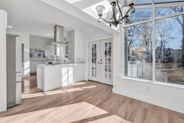 unfurnished dining area featuring sink, french doors, a chandelier, and light wood-type flooring