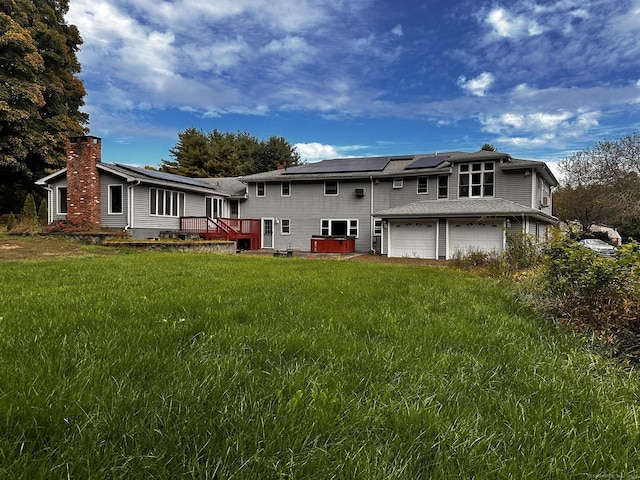 back of property featuring an attached garage, a chimney, solar panels, and a yard