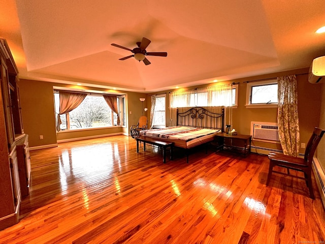 unfurnished bedroom with an AC wall unit, vaulted ceiling, a tray ceiling, and light hardwood / wood-style floors