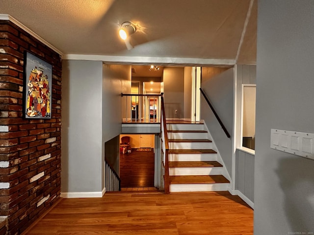 stairway featuring brick wall, a textured ceiling, baseboards, and wood finished floors